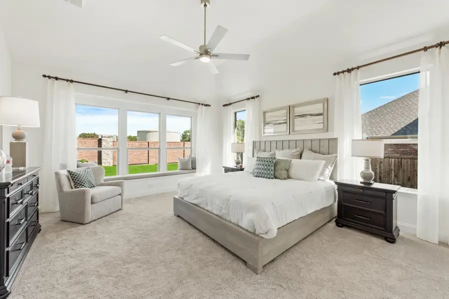 Master bedroom with vaulted ceiling, ceiling fan, window seat, and multiple large windows with natural light