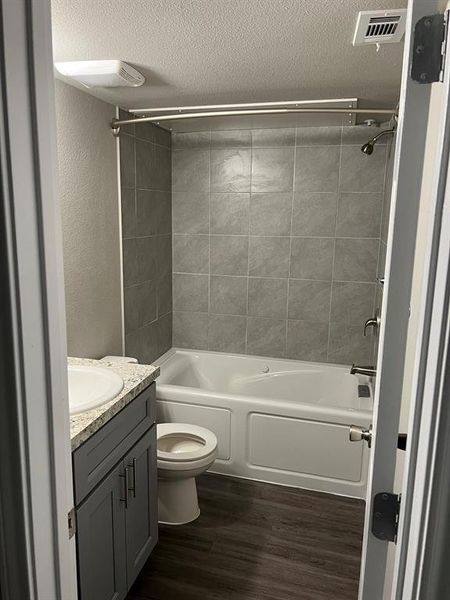 Full bathroom with vanity, hardwood / wood-style flooring, tiled shower / bath combo, toilet, and a textured ceiling