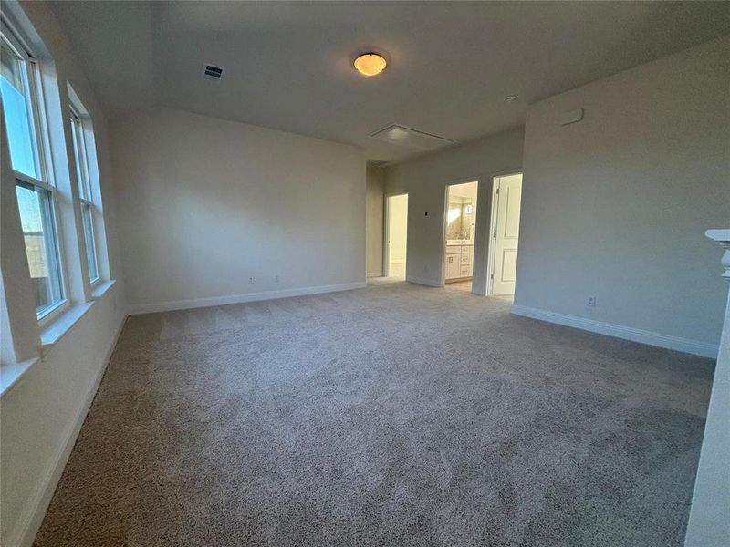 Carpeted empty room with visible vents, vaulted ceiling, and baseboards