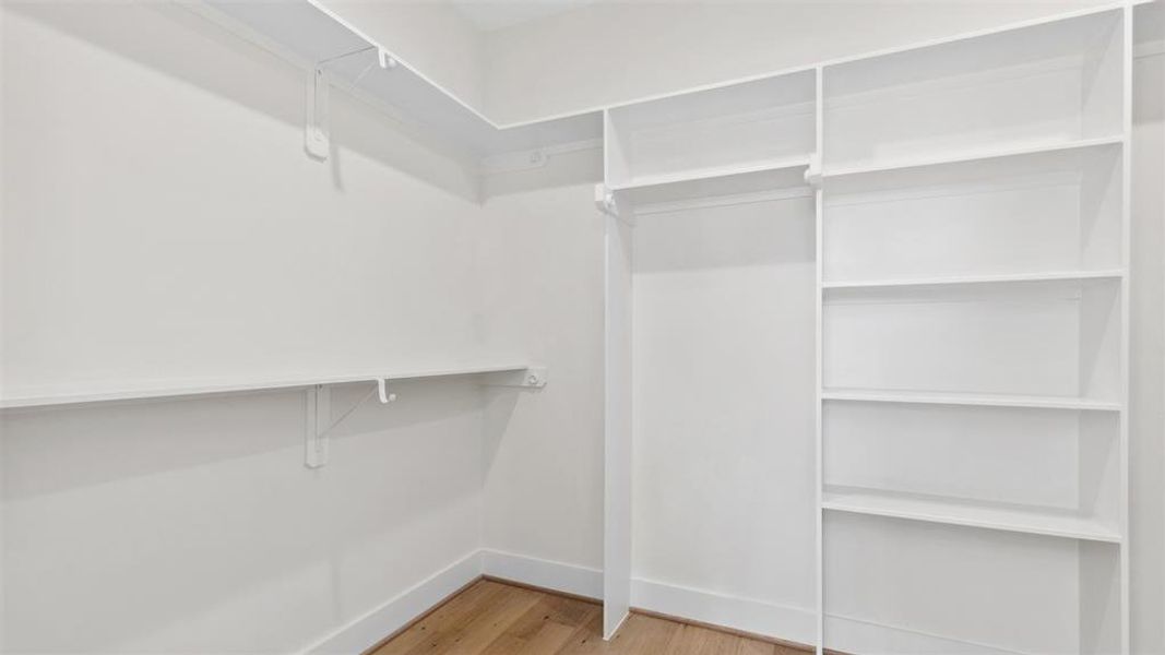 Step into your spacious, clean-lined owners retreat dressed walk-in closet featuring built-in white shelving on one side and multiple hanging rods for ample clothing storage.