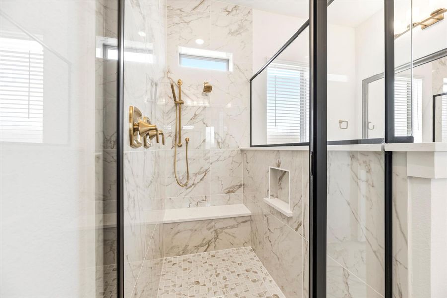 Indulge in the spa-like shower, meticulously finished with custom marble tilework, elegant gold-tone hardware, and built-in bench seating for total comfort.