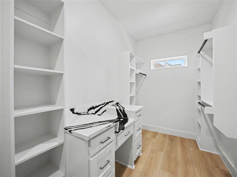 Walk-in closet featuring extensive built-in shelving, hanging rods, and wood-finish flooring Walk-in closet featuring extensive built-in shelving, hanging rods, and wood-finish flooring