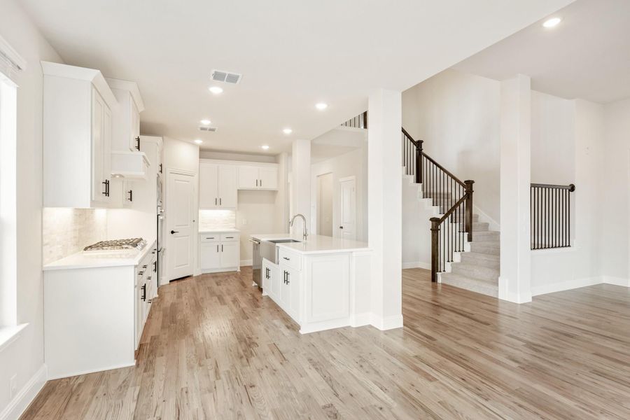 Open kitchen with white cabinets, center island, and wood floors, adjacent to staircase with dark railings
