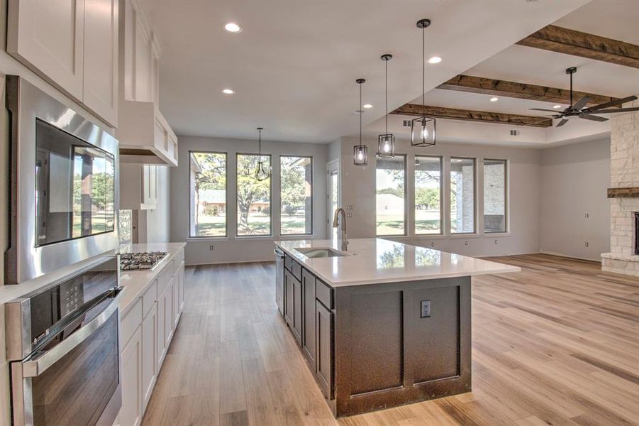 Kitchen with a spacious island, sink, decorative light fixtures, white cabinetry, and appliances with stainless steel finishes