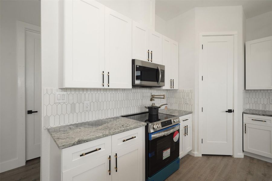 Bright, open living space with modern wood flooring, neutral walls (that seller will professionally paint to the buyer's choosing prior to closing) and ample natural light from large windows. Features a stylish black door and recessed lighting, perfect for a contemporary home.