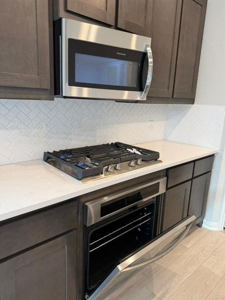 Kitchen featuring dark brown cabinetry, stainless steel appliances, and light wood-style flooring Kitchen featuring dark brown cabinetry, stainless steel appliances, and light wood-style flooring