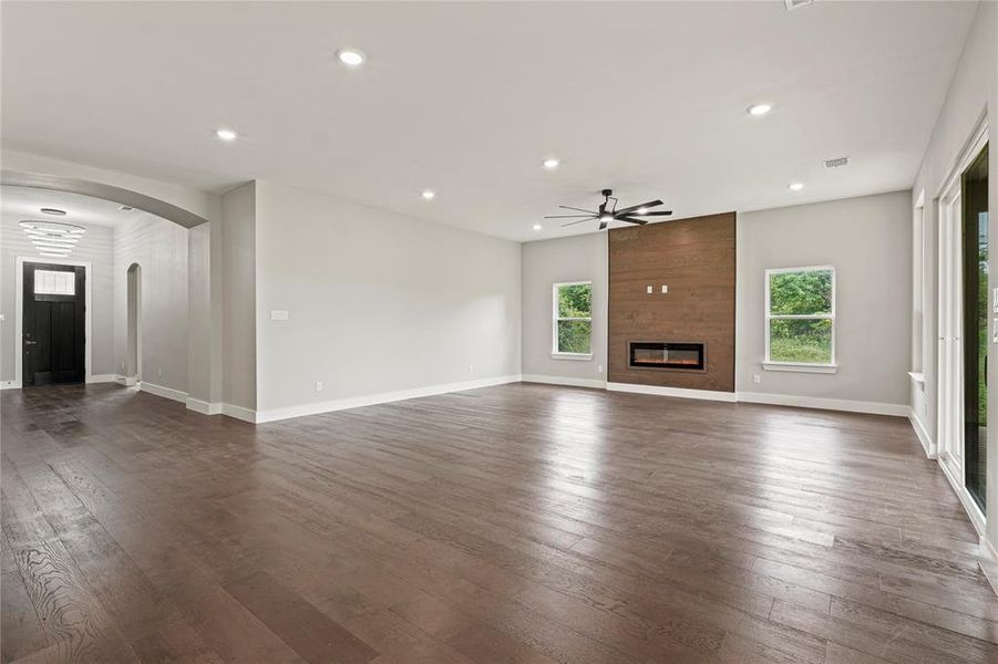Living room featuring ceiling fan, arched walkways, recessed lighting, a large fireplace, and dark wood-style floors