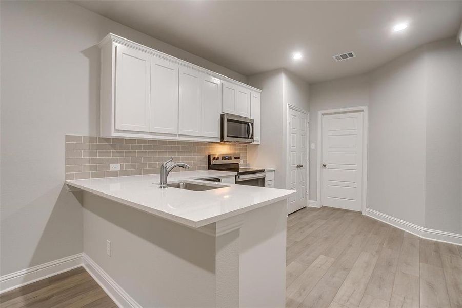 Kitchen with appliances with stainless steel finishes, light countertops, tasteful backsplash, light wood-type flooring, and white cabinetry Kitchen with appliances with stainless steel finishes, light countertops, tasteful backsplash, light wood-type flooring, and white cabinetry