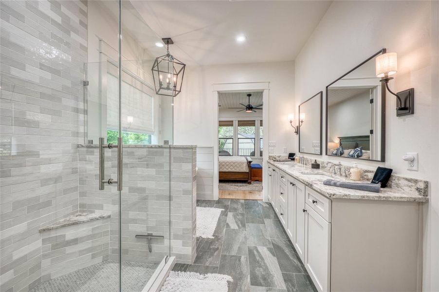 Spacious bathroom featuring a glass-enclosed shower with a built-in bench, dual vanity with undermount sinks, and a stone-finish countertop