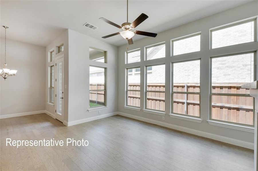 Empty room with ceiling fan with notable chandelier, plenty of natural light, and light hardwood / wood-style floors