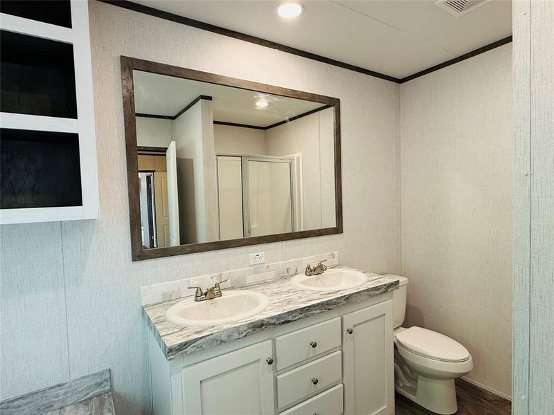 Bathroom featuring double vanity, a shower stall, ornamental molding, and a sink