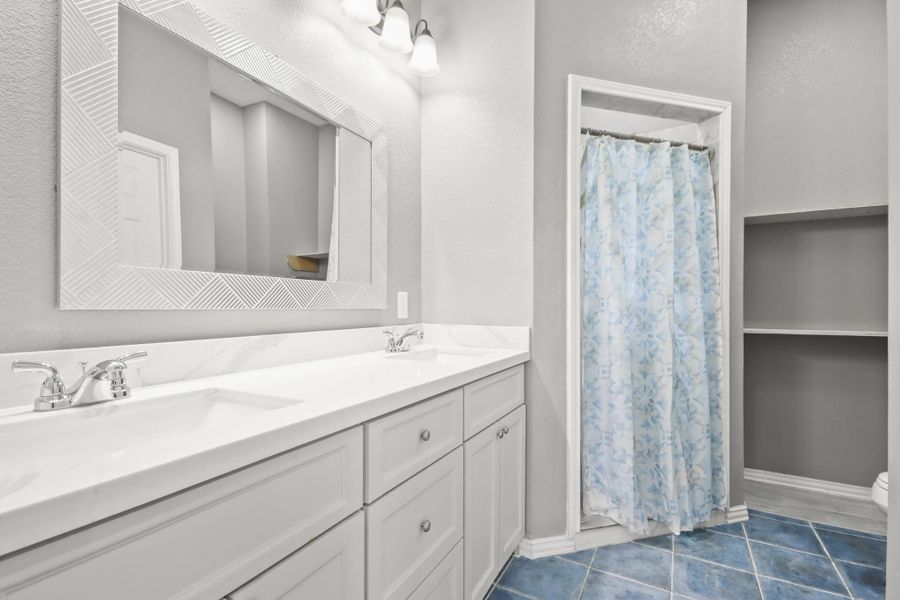 The primary bathroom features a double vanity with sleek faucets, a large framed mirror, and ample storage.