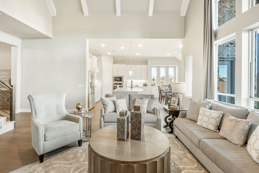 Open-concept living room with high ceilings, gray seating, and kitchen visible in background Open-concept living room with high ceilings, gray seating, and kitchen visible in background