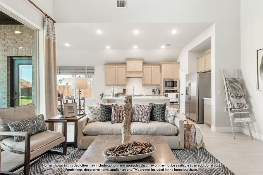 Open-concept living room with beige sofa and patterned pillows, flowing into kitchen with light wood cabinets and stainless appliances.