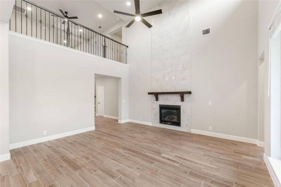 Two-story living room with marble fireplace surround, wood-look floors, and upper balcony railing