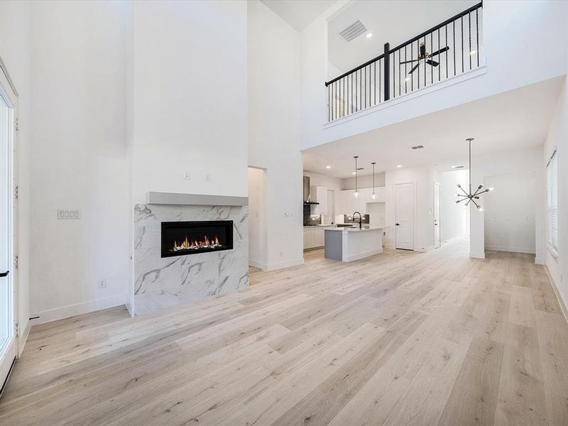 Unfurnished living room with a premium fireplace, light wood-type flooring, a high ceiling, and a chandelier