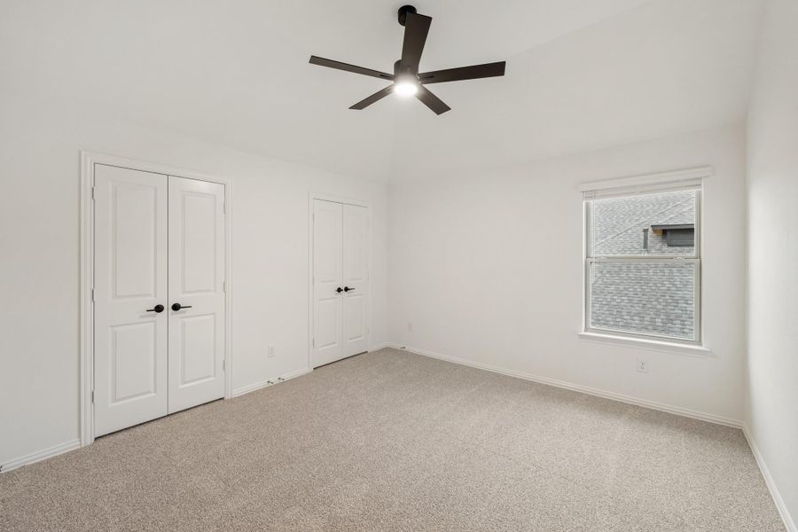Empty bedroom with carpet, ceiling fan, two closets, and a window Empty bedroom with carpet, ceiling fan, two closets, and a window