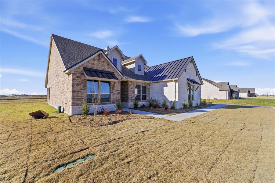 View of front of home with a standing seam roof, a metal roof, a front yard, and brick siding