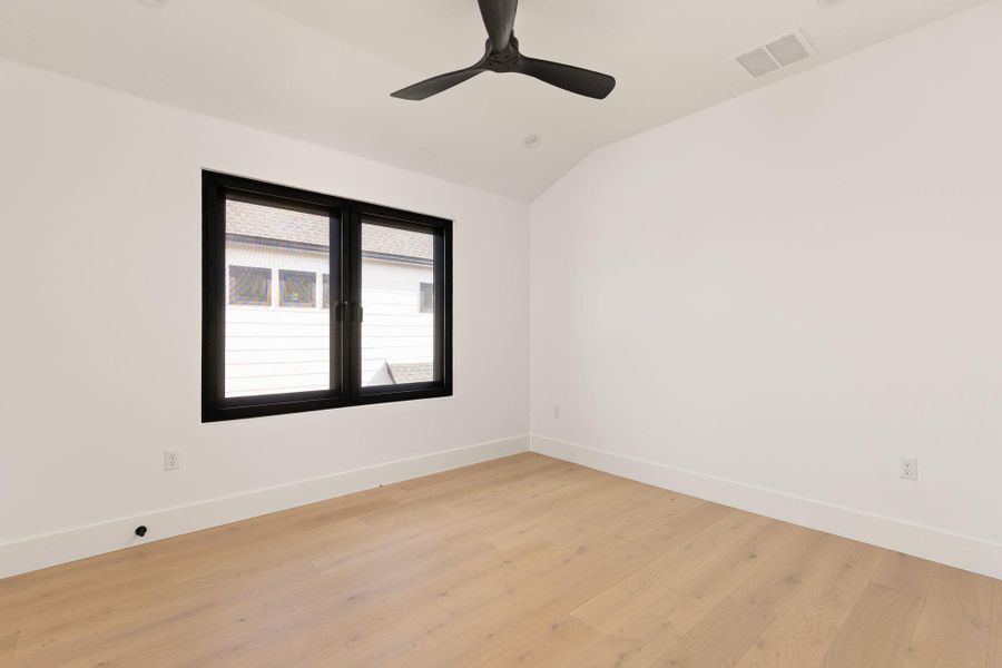 A well-lit bedroom with blonde hardwood flooring features a modern ceiling fan for comfort.