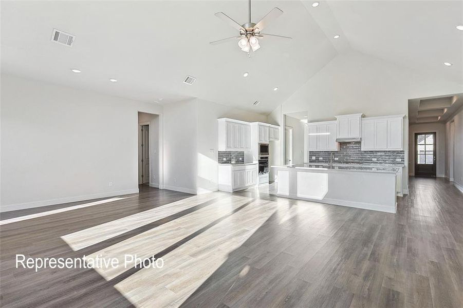 Unfurnished living room featuring ceiling fan, high vaulted ceiling, and wood-type flooring