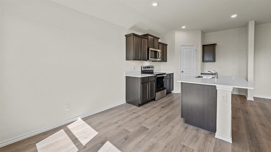 Kitchen featuring stainless steel appliances, a kitchen island with sink, dark wood finish cabinets, light wood-style flooring, and recessed lighting