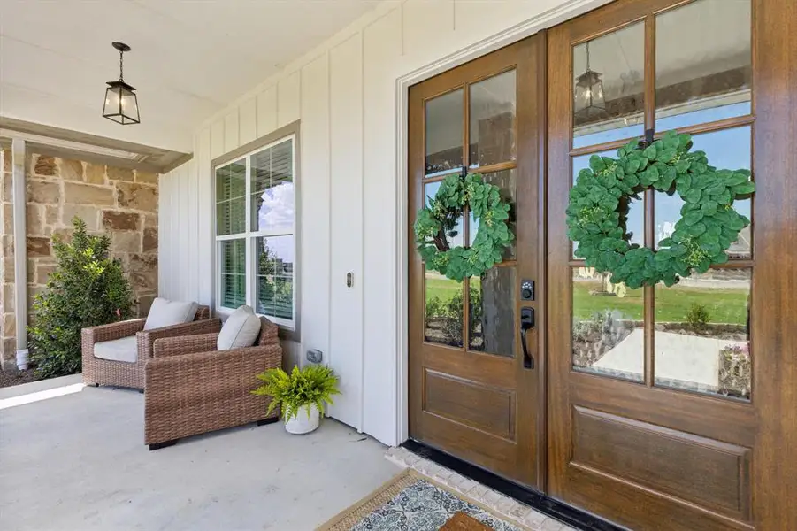 Covered front porch featuring a dual entry door with glass panels, stone accent wall, and a fixed window
