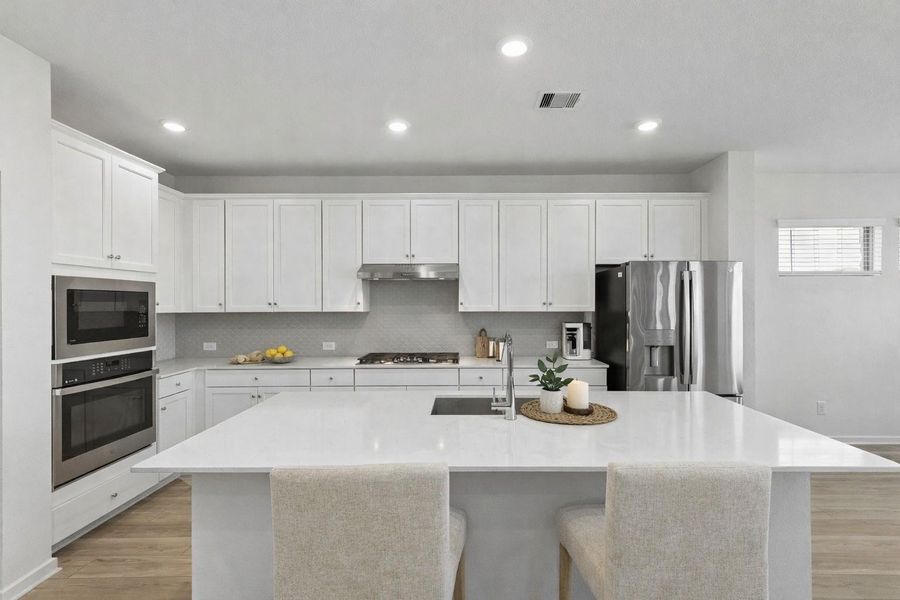 The chef’s kitchen serves as a culinary retreat, centered by a large island with a breakfast bar. Stunning quartz countertops and a designer tile backsplash pair with upgraded Corban-style cabinets to create a stylish and functional space for every meal.