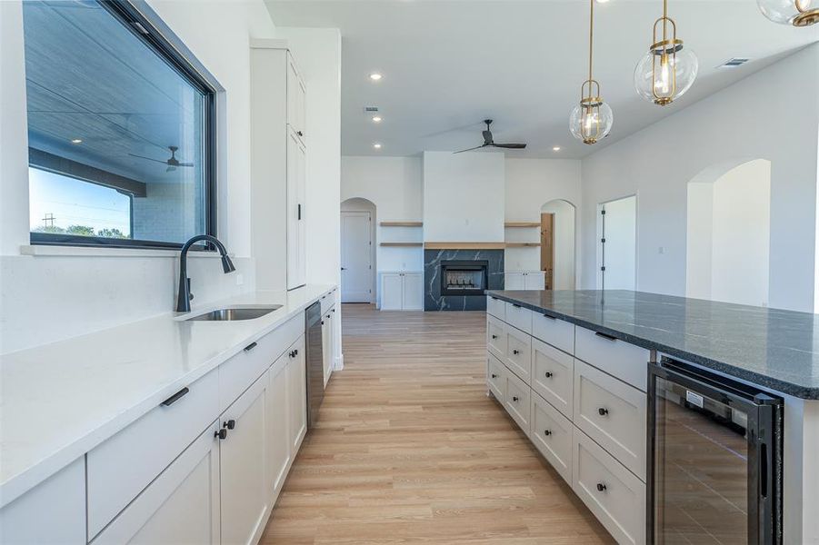 Kitchen with wine cooler, sink, light hardwood / wood-style floors, white cabinetry, and a tiled fireplace