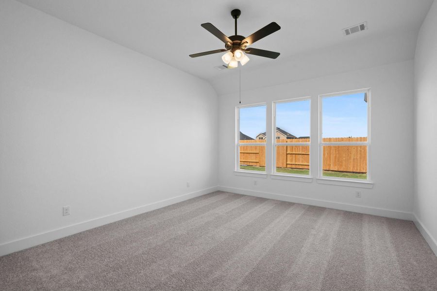 As you enter the primary bedroom, you’re greeted by an abundance of natural light pouring in through large, beautifully framed windows, casting a warm glow on the soft, neutral tones of the walls.