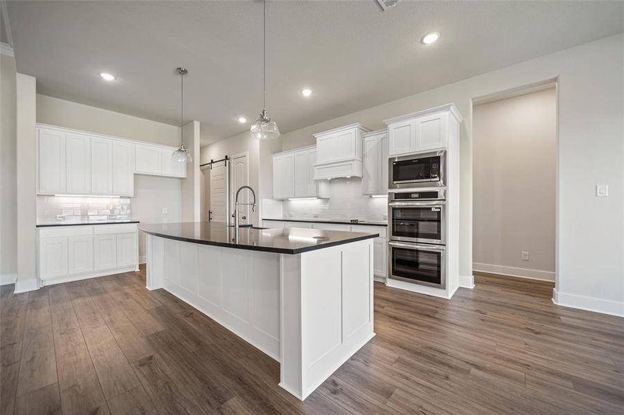 Kitchen with tasteful backsplash, white cabinetry, a barn door, hanging light fixtures, and appliances with stainless steel finishes Kitchen with tasteful backsplash, white cabinetry, a barn door, hanging light fixtures, and appliances with stainless steel finishes