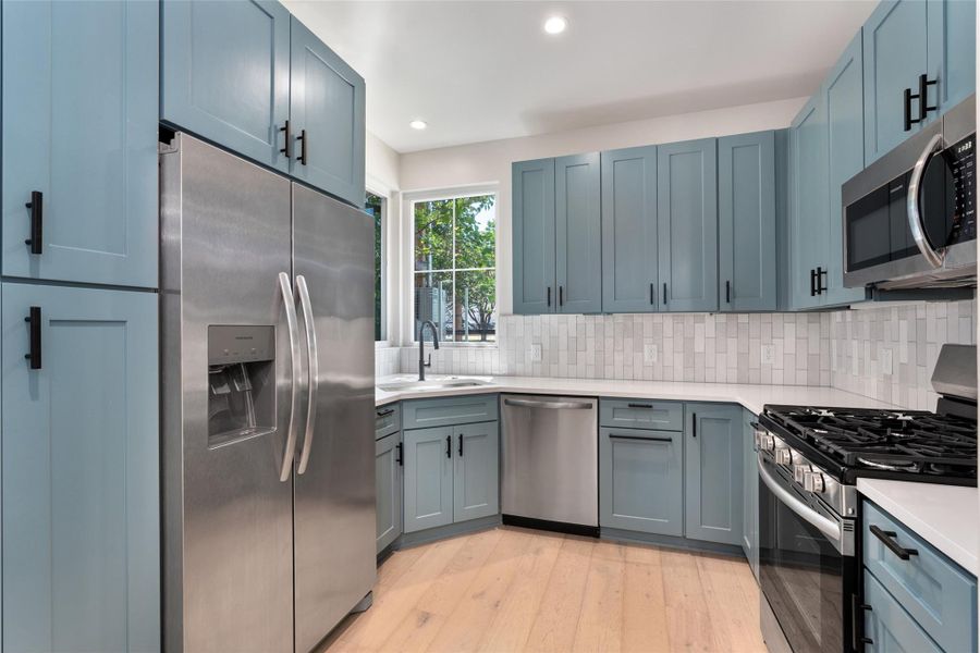 Kitchen featuring shaker-style cabinetry with matte black hardware, stainless steel appliances, light wood-finish flooring, white countertops, and a subway tile backsplash Kitchen featuring shaker-style cabinetry with matte black hardware, stainless steel appliances, light wood-finish flooring, white countertops, and a subway tile backsplash