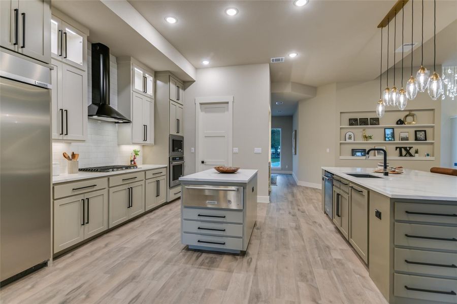 Kitchen featuring a kitchen island with sink, pendant lighting, glass insert cabinets, light stone counters, and recessed lighting Kitchen featuring a kitchen island with sink, pendant lighting, glass insert cabinets, light stone counters, and recessed lighting