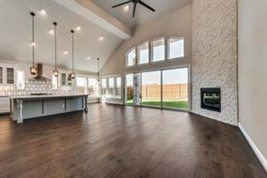 Unfurnished living room featuring ceiling fan, high vaulted ceiling, beamed ceiling, a fireplace, and dark hardwood / wood-style floors