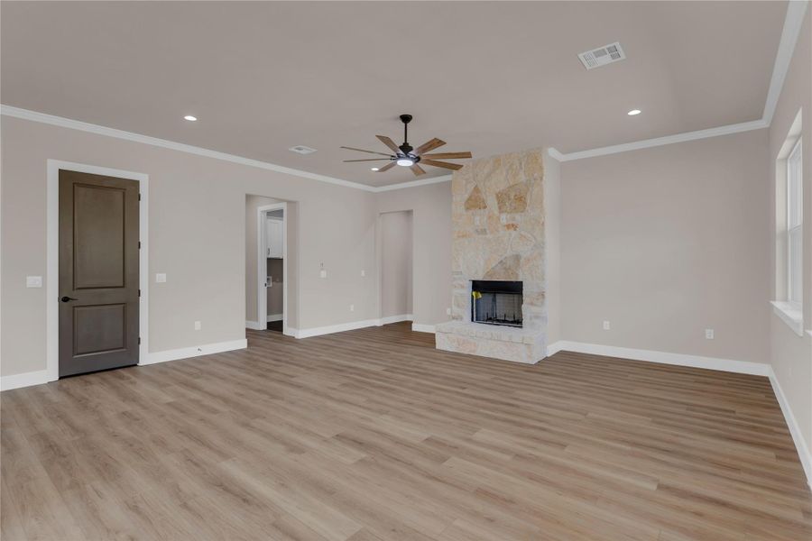 Unfurnished living room featuring ceiling fan, ornamental molding, a large fireplace, light wood-type flooring, and recessed lighting
