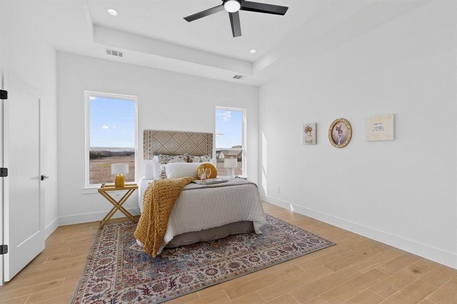 Bedroom featuring wood finish floors, a raised ceiling, ceiling fan, multiple windows, and recessed lighting