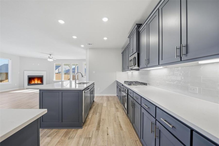 Kitchen with a lit fireplace, open floor plan, an island with sink, recessed lighting, and light wood-style flooring Kitchen with a lit fireplace, open floor plan, an island with sink, recessed lighting, and light wood-style flooring