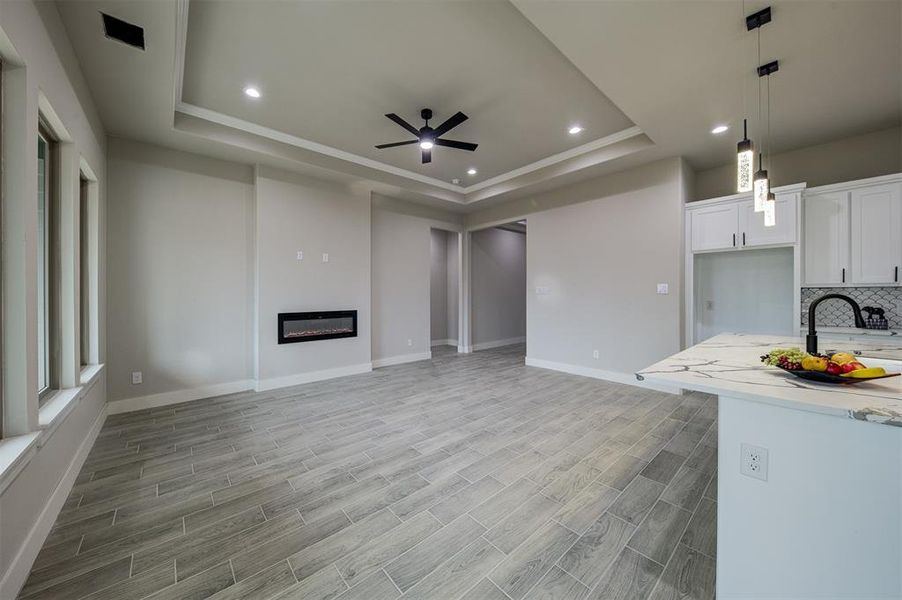 Kitchen featuring light hardwood / wood-style flooring, white cabinetry, decorative backsplash, decorative light fixtures, and a raised ceiling