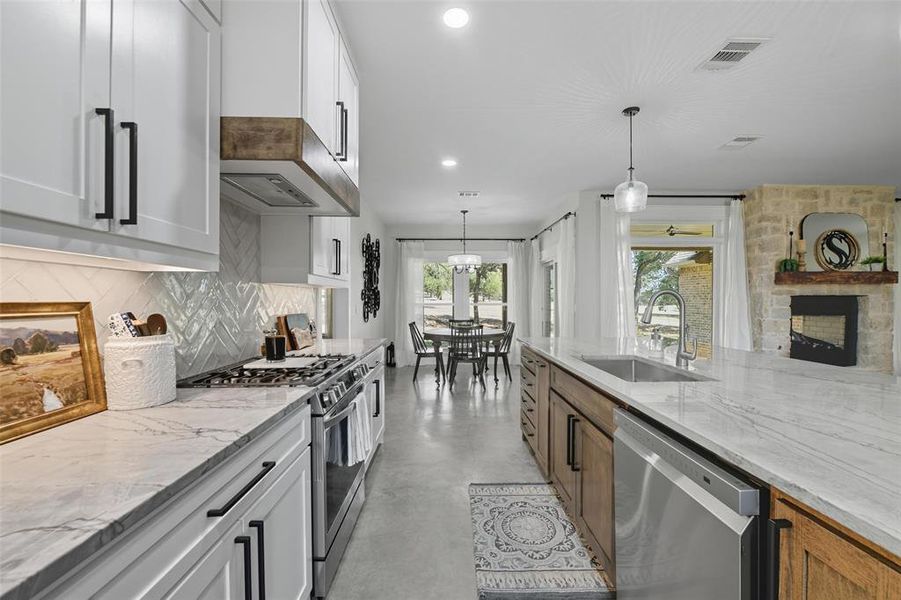 Kitchen with stainless steel appliances, finished concrete floors, light stone countertops, decorative light fixtures, and white cabinetry Kitchen with stainless steel appliances, finished concrete floors, light stone countertops, decorative light fixtures, and white cabinetry