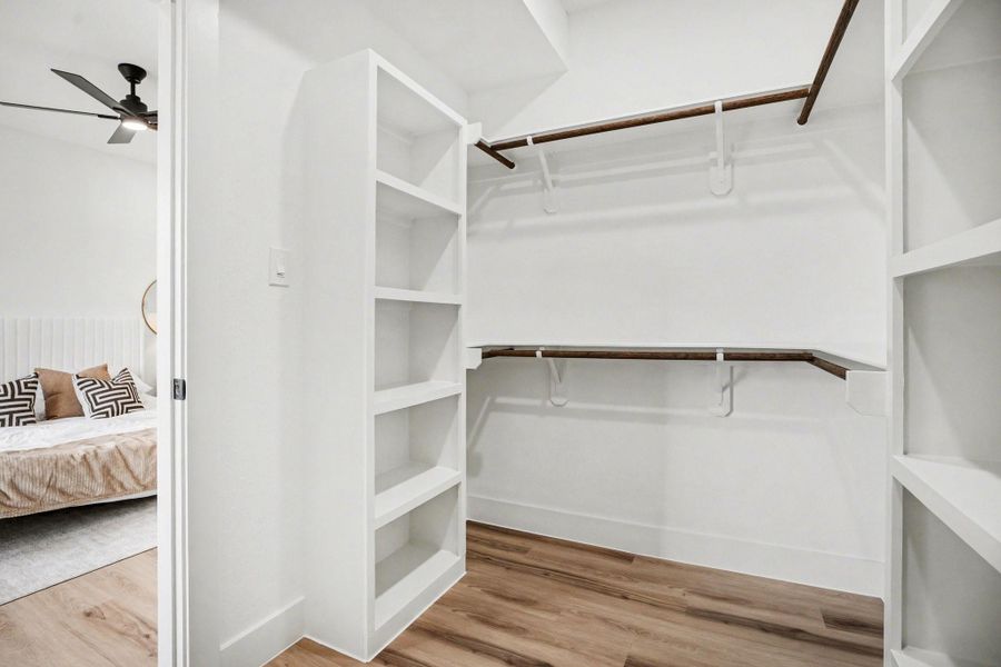 This photo shows a spacious walk-in closet with white shelving and wooden rods for hanging clothes.