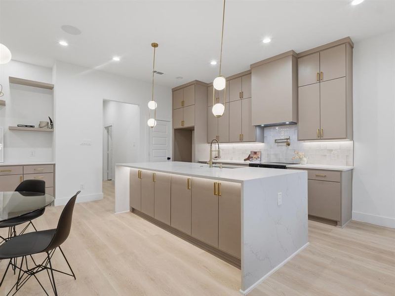 Kitchen featuring light wood finished floors, a kitchen island with sink, decorative light fixtures, light stone counters, and backsplash Kitchen featuring light wood finished floors, a kitchen island with sink, decorative light fixtures, light stone counters, and backsplash