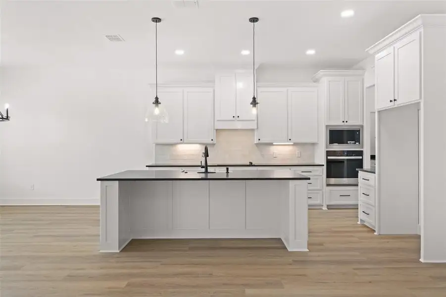 Kitchen featuring dark countertops, a kitchen island with sink, stainless steel appliances, light wood-type flooring, and white cabinets