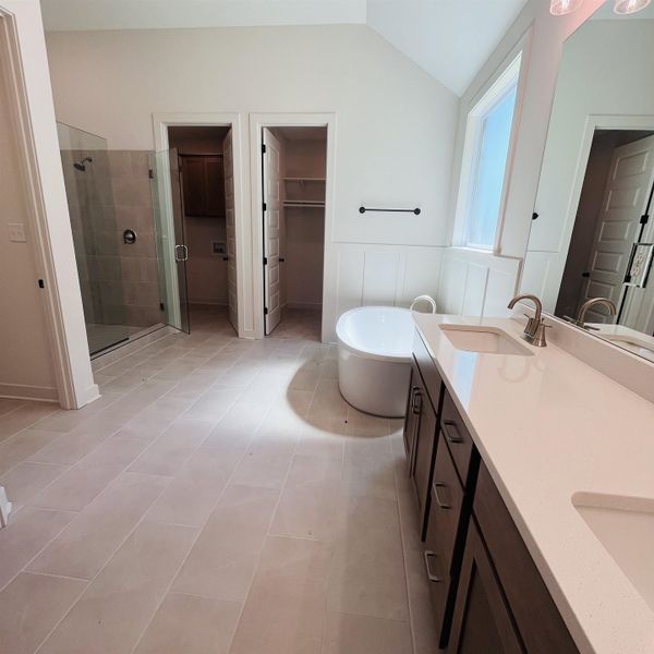 Vaulted ceiling, glass-enclosed shower, freestanding soaking tub, dual vanity with undermount sinks, and plank tile flooring