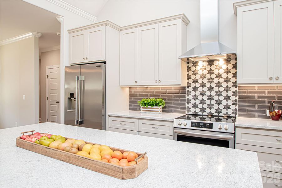 This stunning kitchen with vaulted ceilings showcases stainless steel appliances, granite countertops, a stylish gray subway tile backsplash, and soft-close cabinetry with convenient pull-out drawers.