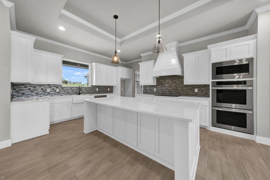 Kitchen with a tray ceiling, stainless steel appliances, double oven, custom range hood, and backsplash