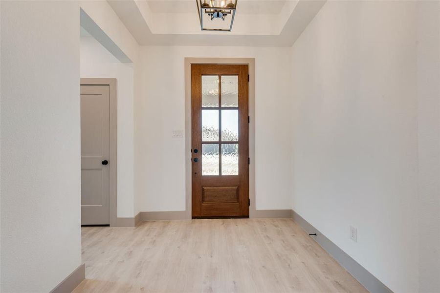 Entryway featuring a tray ceiling, a chandelier, and light hardwood / wood-style flooring