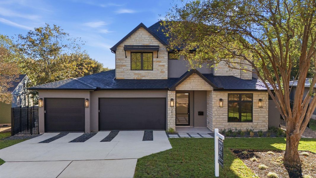 View of front of home with stone siding, driveway, an attached garage, and a shingled roof