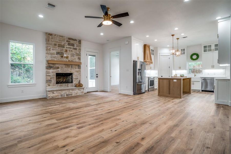 Unfurnished living room with a stone fireplace, plenty of natural light, ceiling fan with notable chandelier, and light wood-type flooring