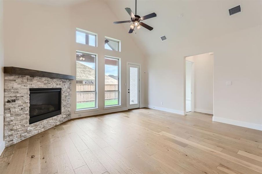 Unfurnished living room featuring a stone fireplace, light hardwood / wood-style flooring, ceiling fan, and high vaulted ceiling