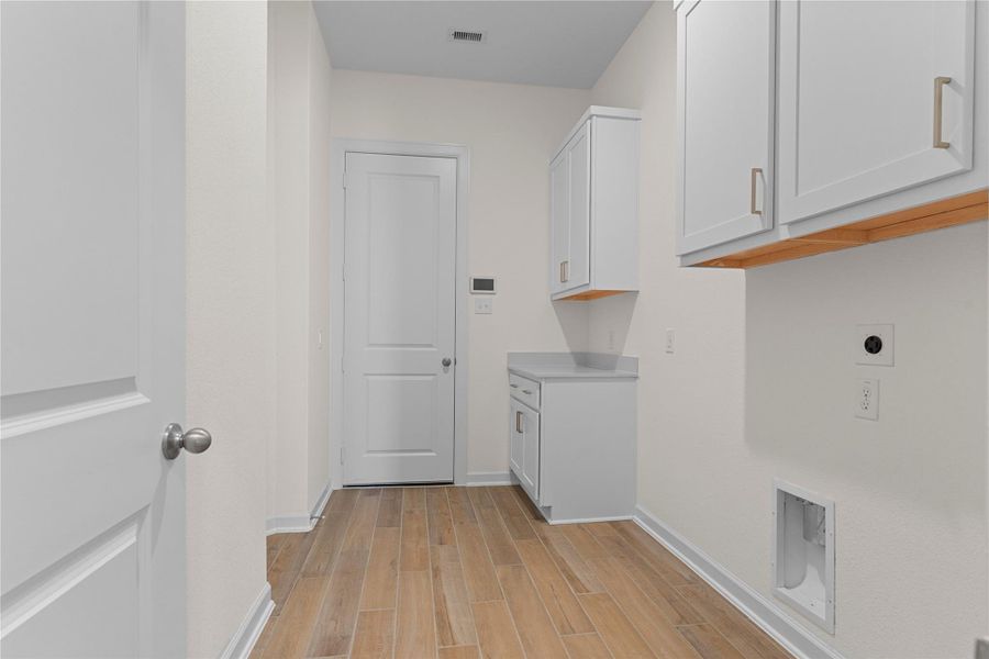 The utility room offers excellent functionality with dedicated washer and dryer connections, built in cabinetry for storage, and durable wood like tile flooring, making everyday tasks both easy and organized.