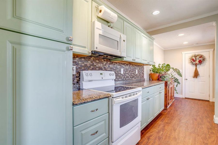 Kitchen featuring white appliances, crown molding, recessed lighting, light wood-type flooring, and backsplash
